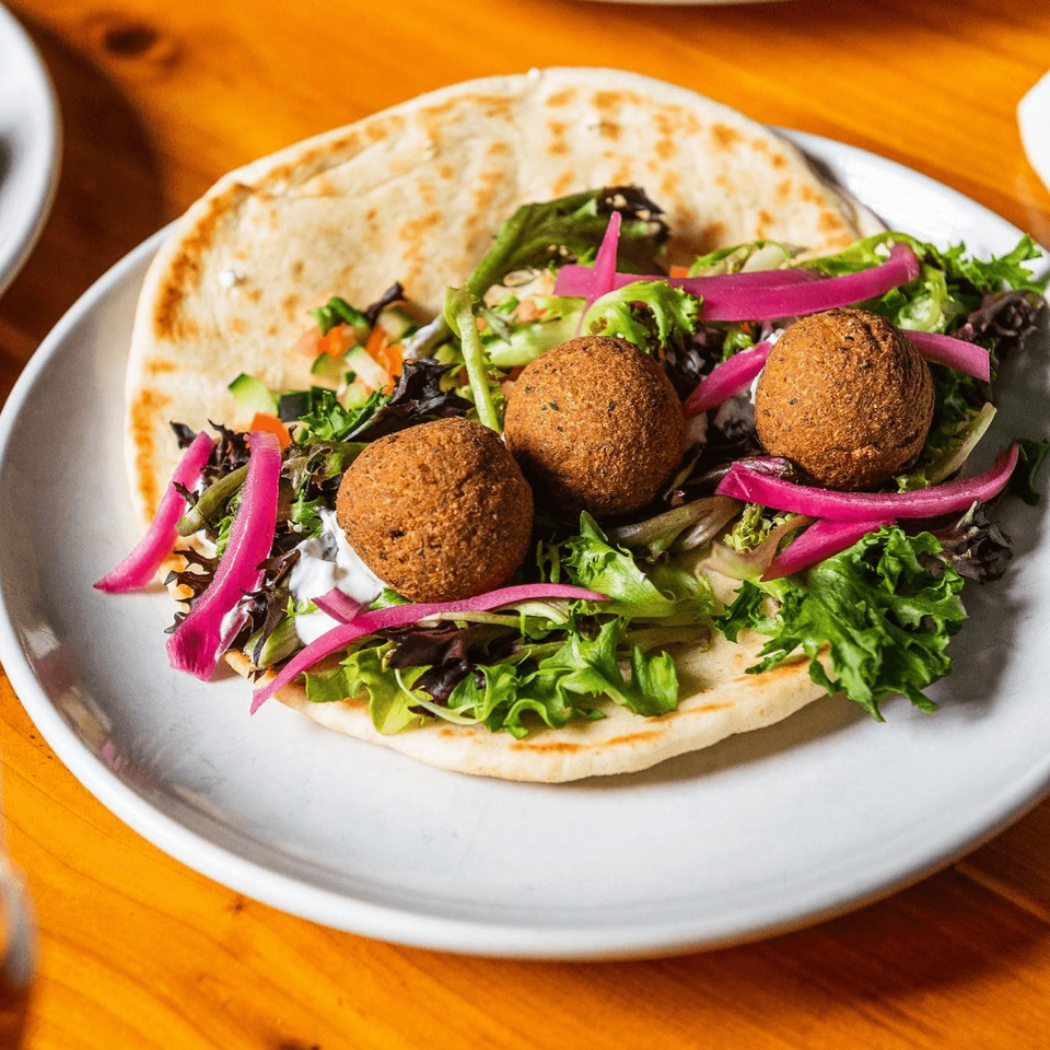A falafel pita with lettuce, pickled red onions, and diced vegetables on a white plate.