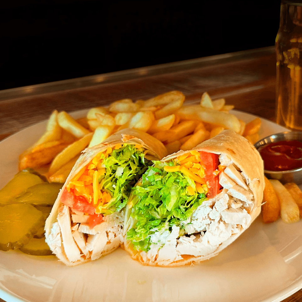 A chicken wrap cut in half, served with french fries, pickles, and ketchup at Brookland Pint.