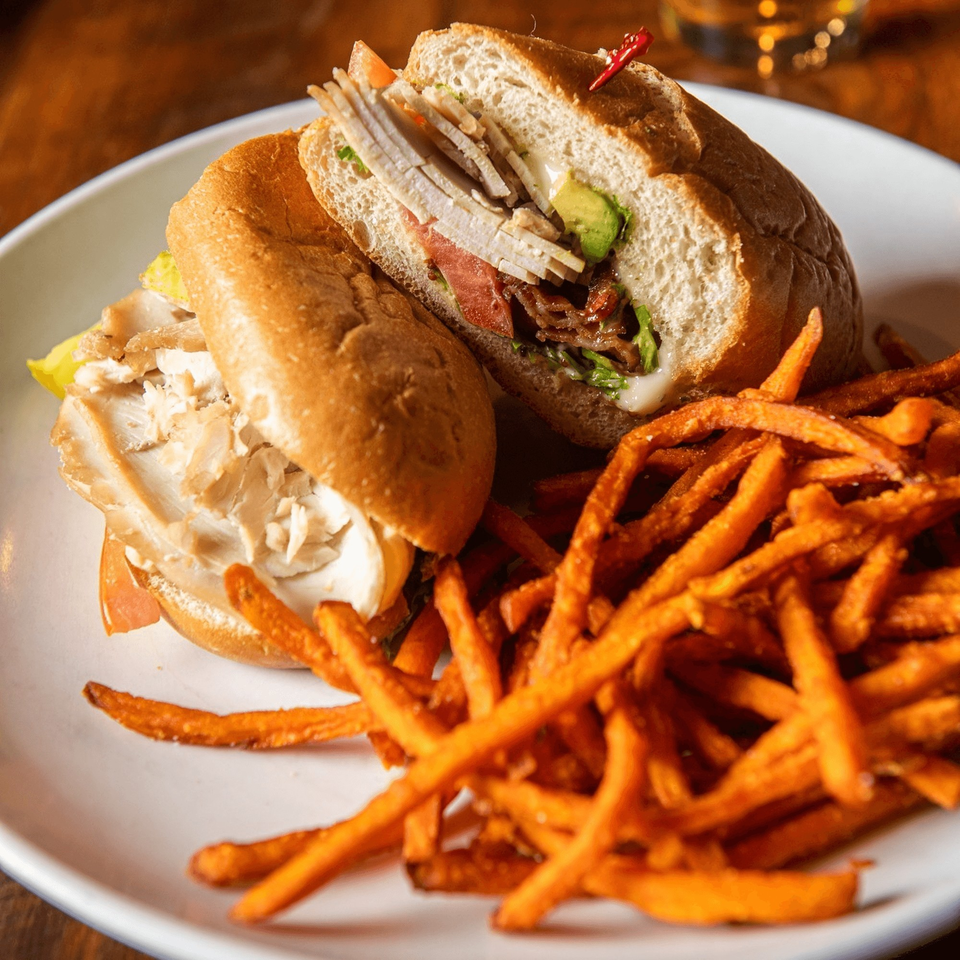 A turkey and avocado sandwich with bacon and tomato, served with a side of sweet potato fries.