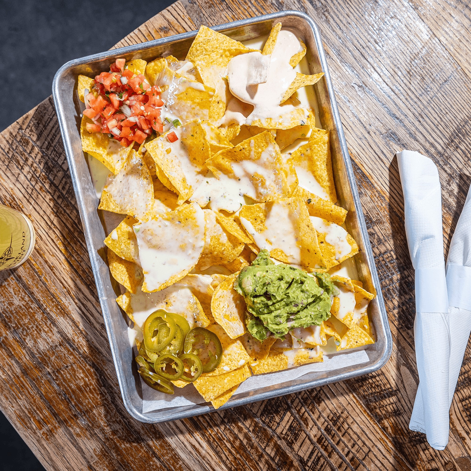 Overhead view of a tray of nachos with cheese, salsa, guacamole, and jalapeños on a wooden table.