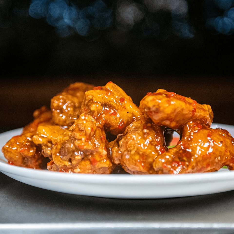 A white plate piled high with glistening, orange-glazed chicken wings, speckled with red chili flakes.